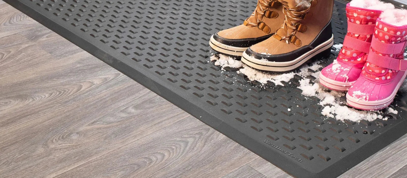 Person wearing brown boots and pink children's boots stepping onto a textured mat.
