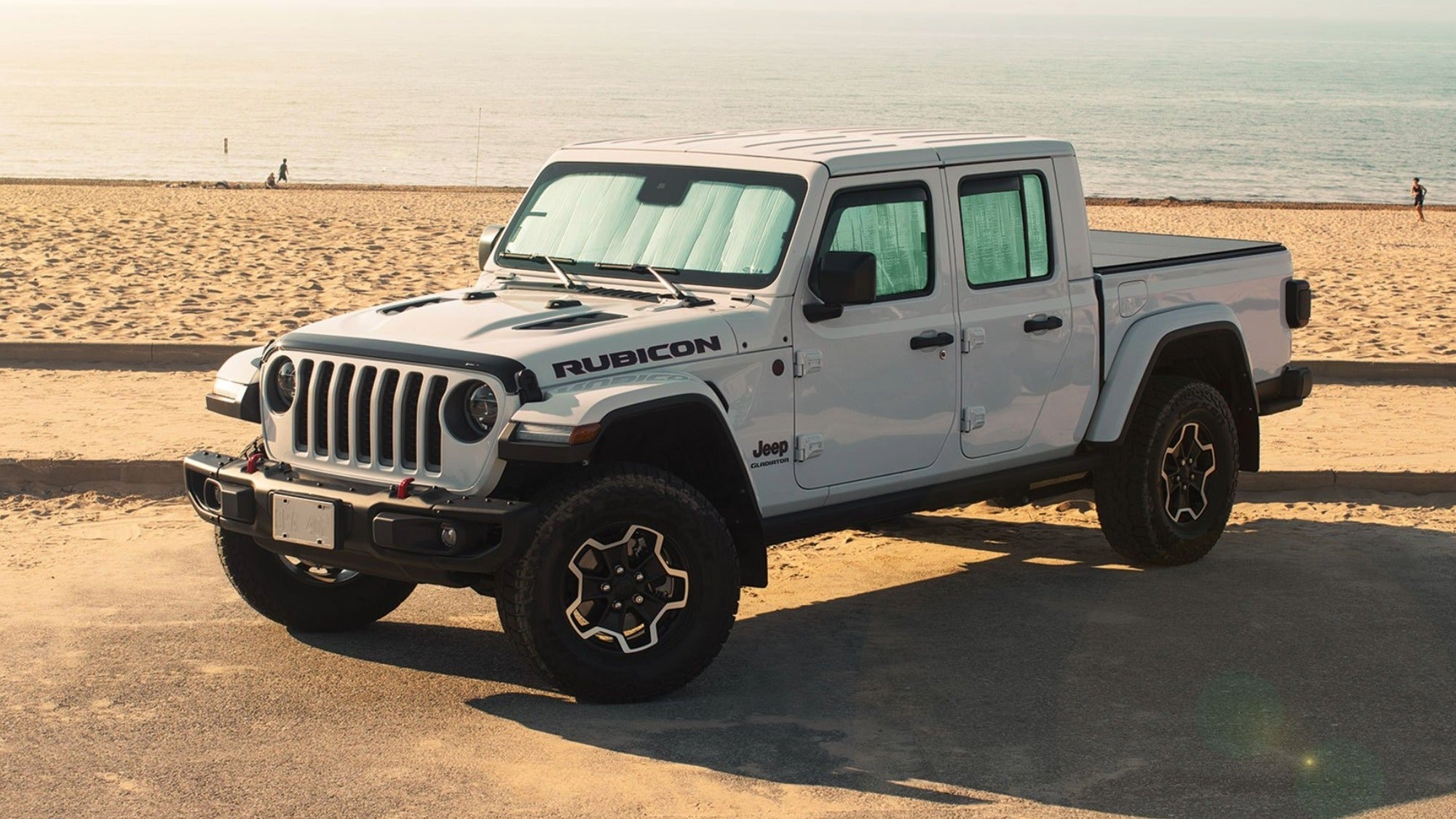 White Jeep Gladiator Rubicon parked on a sandy beach with ocean in the background