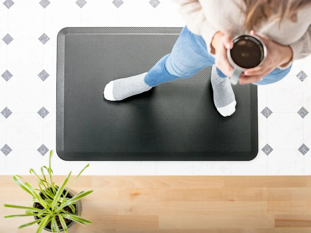 Person standing on a black anti-fatigue mat with a plant and cup in the foreground.